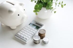 A white piggy bank, electronic calculator, and coins