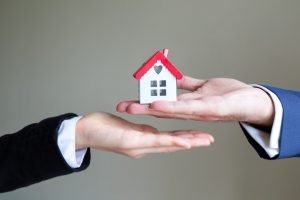 one person handing a small house to another person
